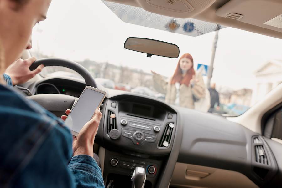 Young driver looking distracted at his smart phone while about to hit a pedestrian crossing the road