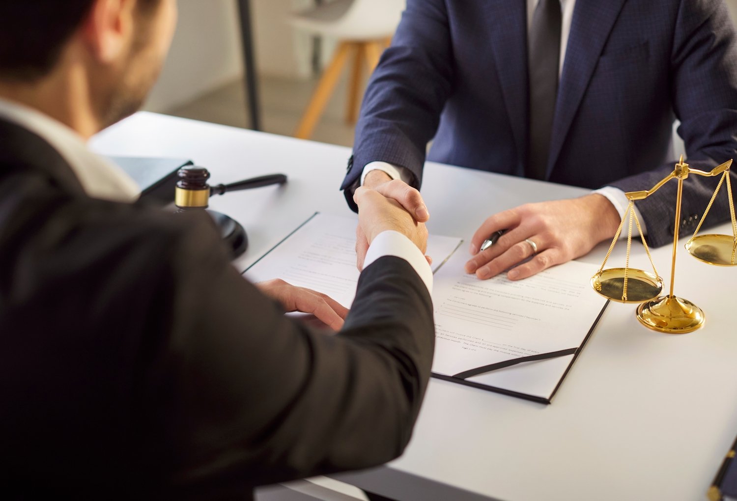 Lawyers shaking hands over a desk with a gavel in the background