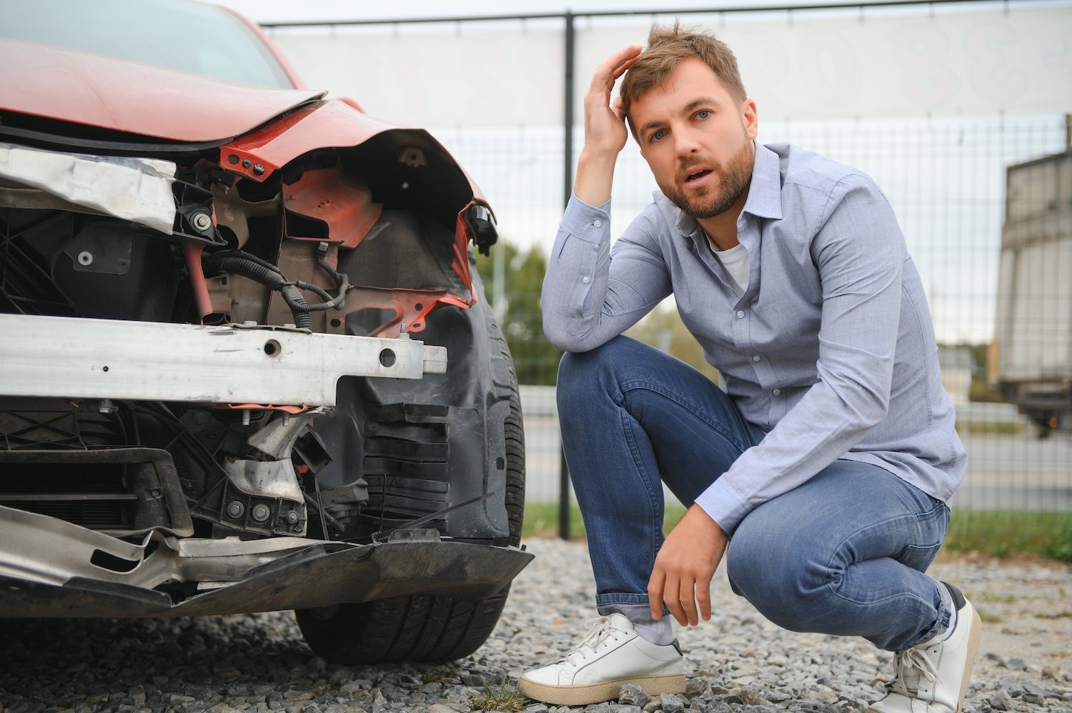 Injured driver kneeling next to his car following a car crash