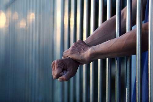 Jail cell and inmate hands sticking through the bars