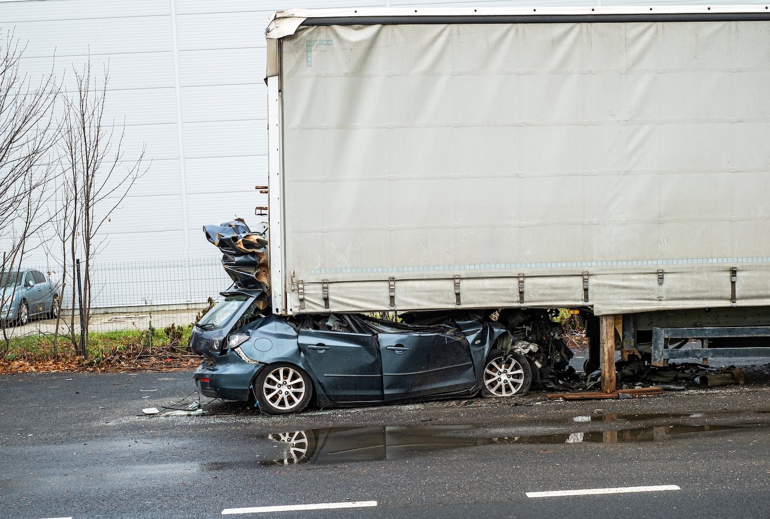 Blue sedan under a white truck following a crash on a cloudy day