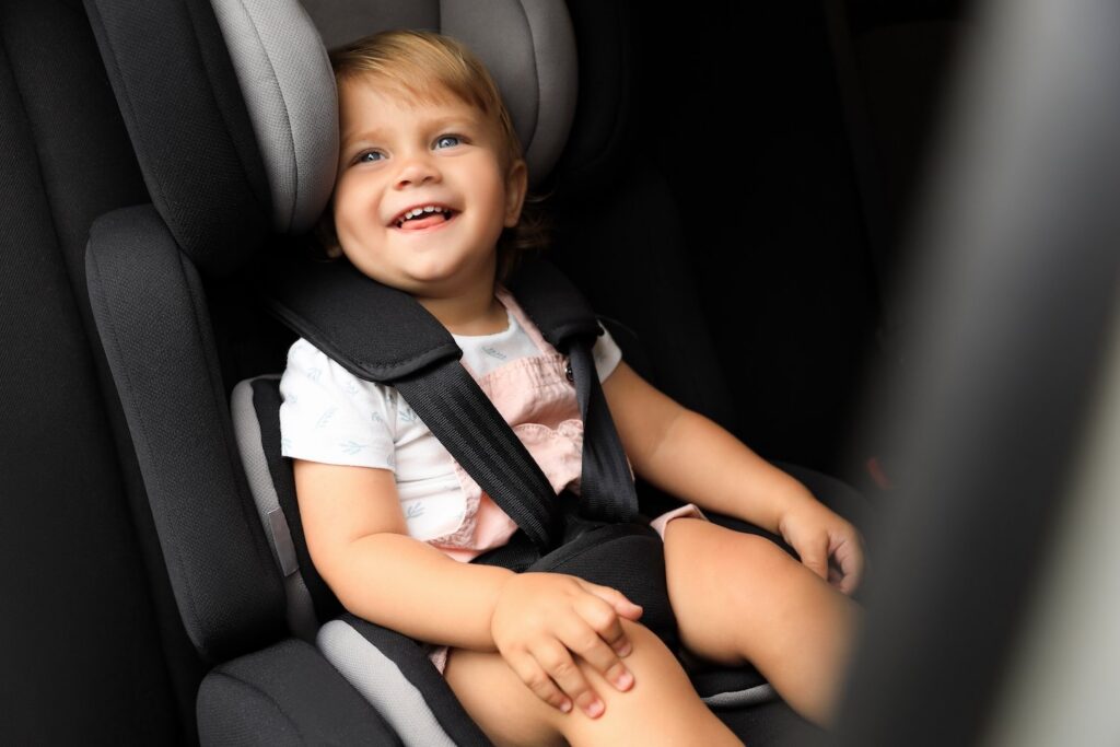 Smiling toddler strapped into a car seat in a van